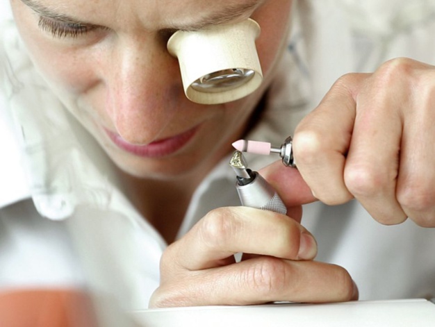 Patience et savoir-faire : une horlogère des ateliers NOMOS exécute le biseautage des arêtes du coq avec une concentration maximale.